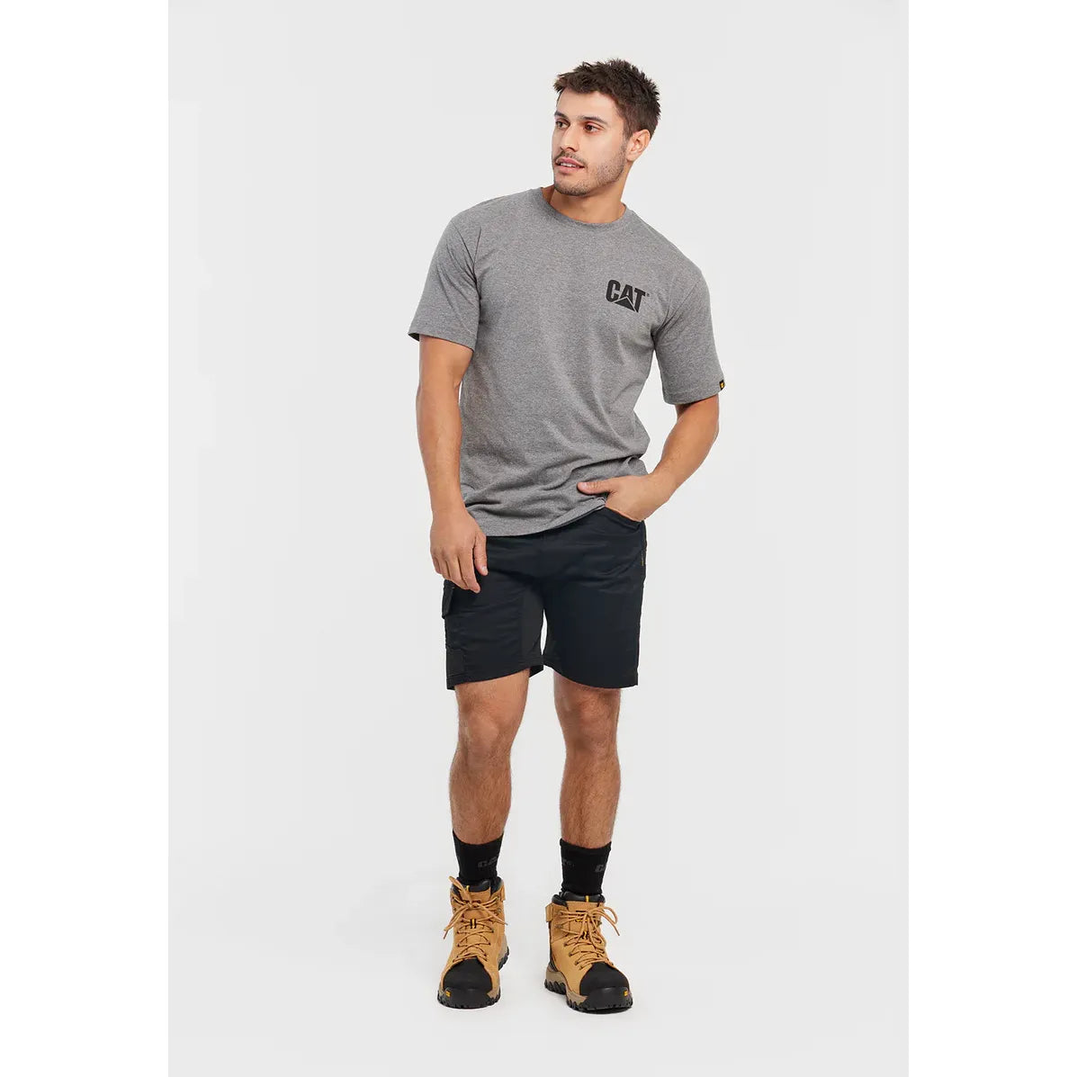 Man wearing a gray t-shirt with a logo, black shorts, and brown boots on a white background