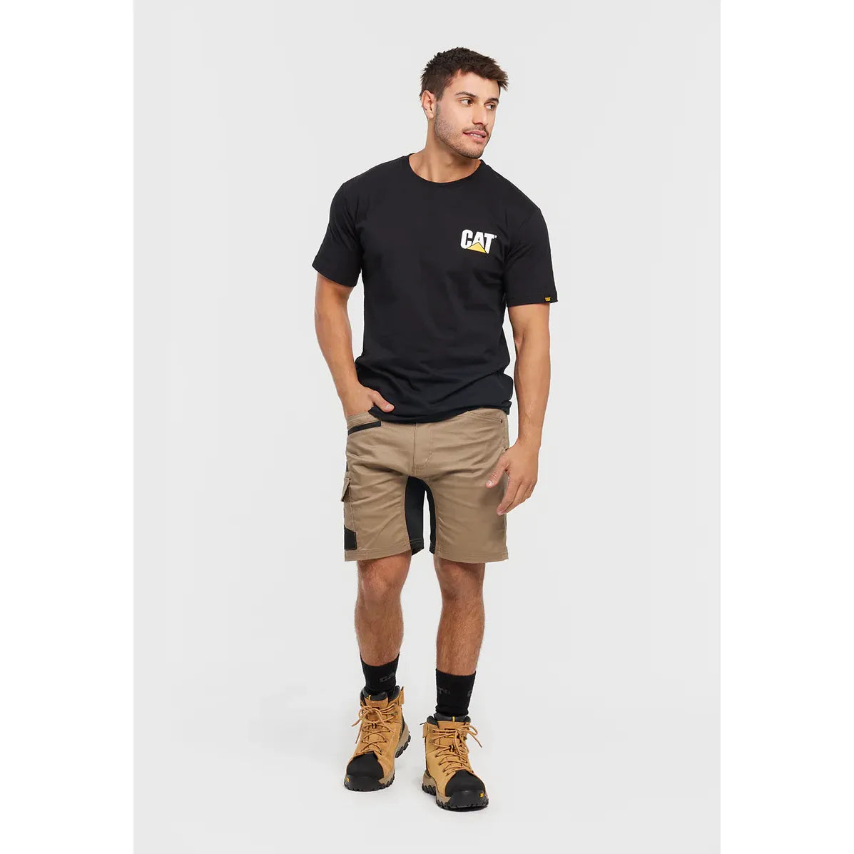 Man wearing a black t-shirt with a logo, beige cargo shorts, and work boots on a white background