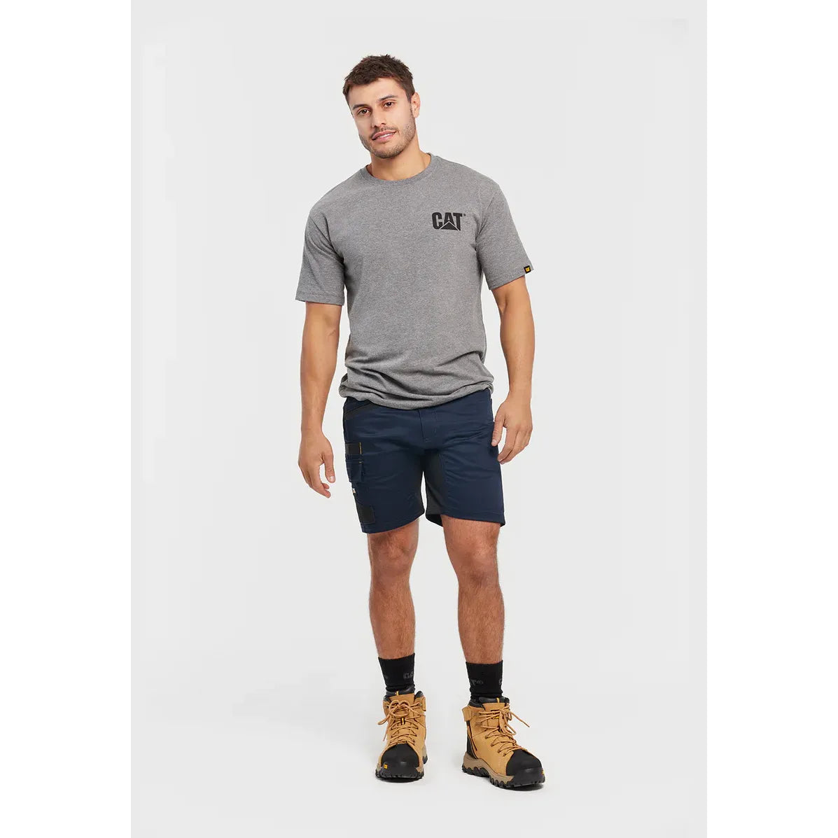 Man wearing a gray t-shirt with a logo, navy shorts, and brown boots on a white background